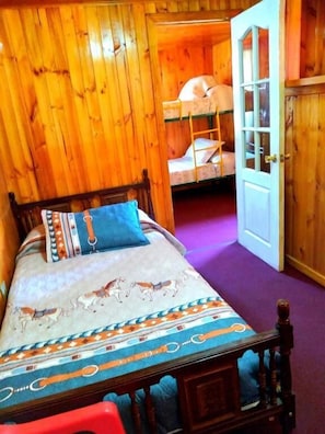 Una habitación de madera con una cama, literas y una puerta.