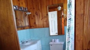 A bathroom with wooden walls, a white sink, a toilet, and a mirror above it. - Hostal Gomero (Santa Cruz)