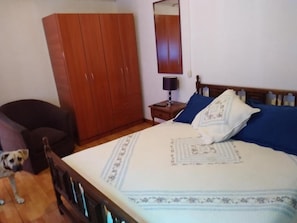 Un dormitorio con una cama, un armario de madera, una mesita de noche, una lámpara y un perro.