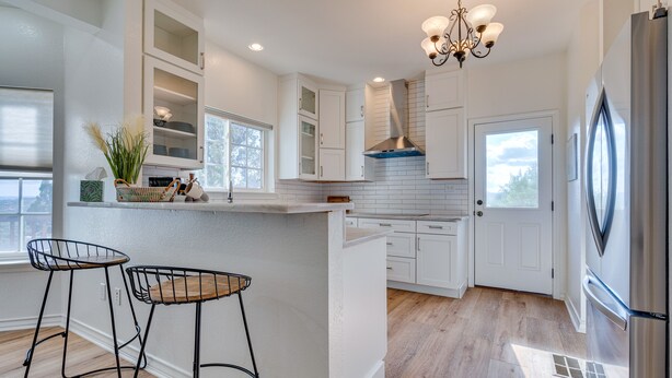 A modern kitchen with white cabinetry, a central island, two bar stools, and a stainless steel refrigerator. - Jonestown Retreat w/ Deck: 6 Mi to Lake Travis! (Jonestown)