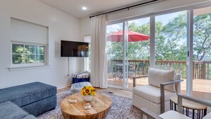A modern living room with a large TV, a wooden coffee table with a vase of sunflowers, a grey sofa, and a beige armchair. - Jonestown Retreat w/ Deck: 6 Mi to Lake Travis! (Jonestown)
