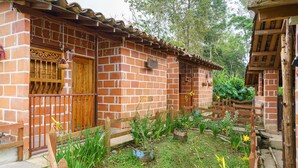 A rustic brick building with a wooden door and a small garden area with potted plants and a wooden fence. - Ciudadela el Artesano  (Carolina del Príncipe)