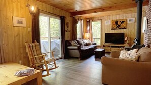 En mysig stuga med träpanel på väggarna, en soffa, en tv och en öppen spis.