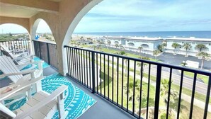 A balcony with white chairs and a blue patterned floor, overlooking a beach and a parking lot with palm trees. - Ponce Inlet 6th Floor Ocean View Corner Unit- 2bdrm 2bath- Non Drive Beach  (Ponce Inlet)