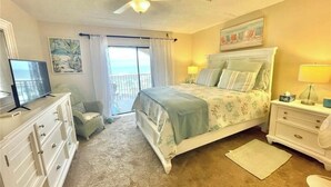 A bedroom with a bed, a dresser, a television, a window with curtains, and a ceiling fan. - Ponce Inlet 6th Floor Ocean View Corner Unit- 2bdrm 2bath- Non Drive Beach  (Ponce Inlet)