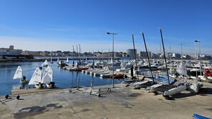 A marina with multiple boats docked, a clear sky, and buildings in the background. - Casa Sebastian (L'Escala)