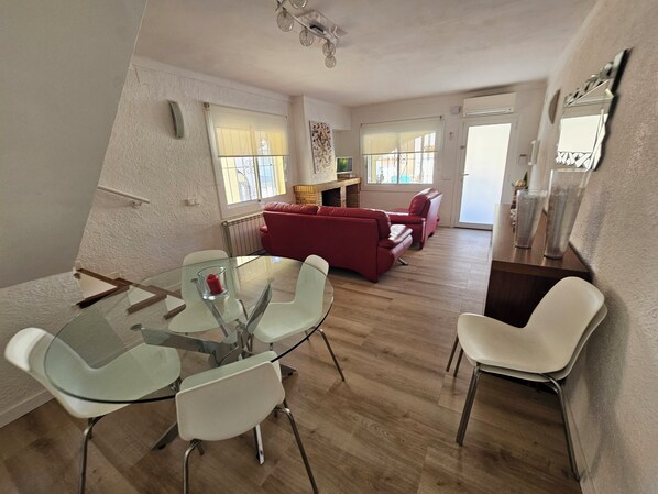 A modern living room with a glass dining table, red leather sofas, and a wooden floor.