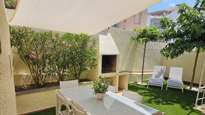 A patio area with a glass-top table and chairs, surrounded by green artificial turf and potted plants. - Casa Sebastian (L'Escala)