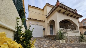 A building with a stone-paved entrance, a white door, and a sign reading "CASA SERRA STAND". - Casa Sebastian (L'Escala)