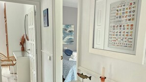 A hallway with a white wardrobe, a framed nautical chart, and a bed with a blue patterned bedspread in the background. - Casa Sebastian (L'Escala)