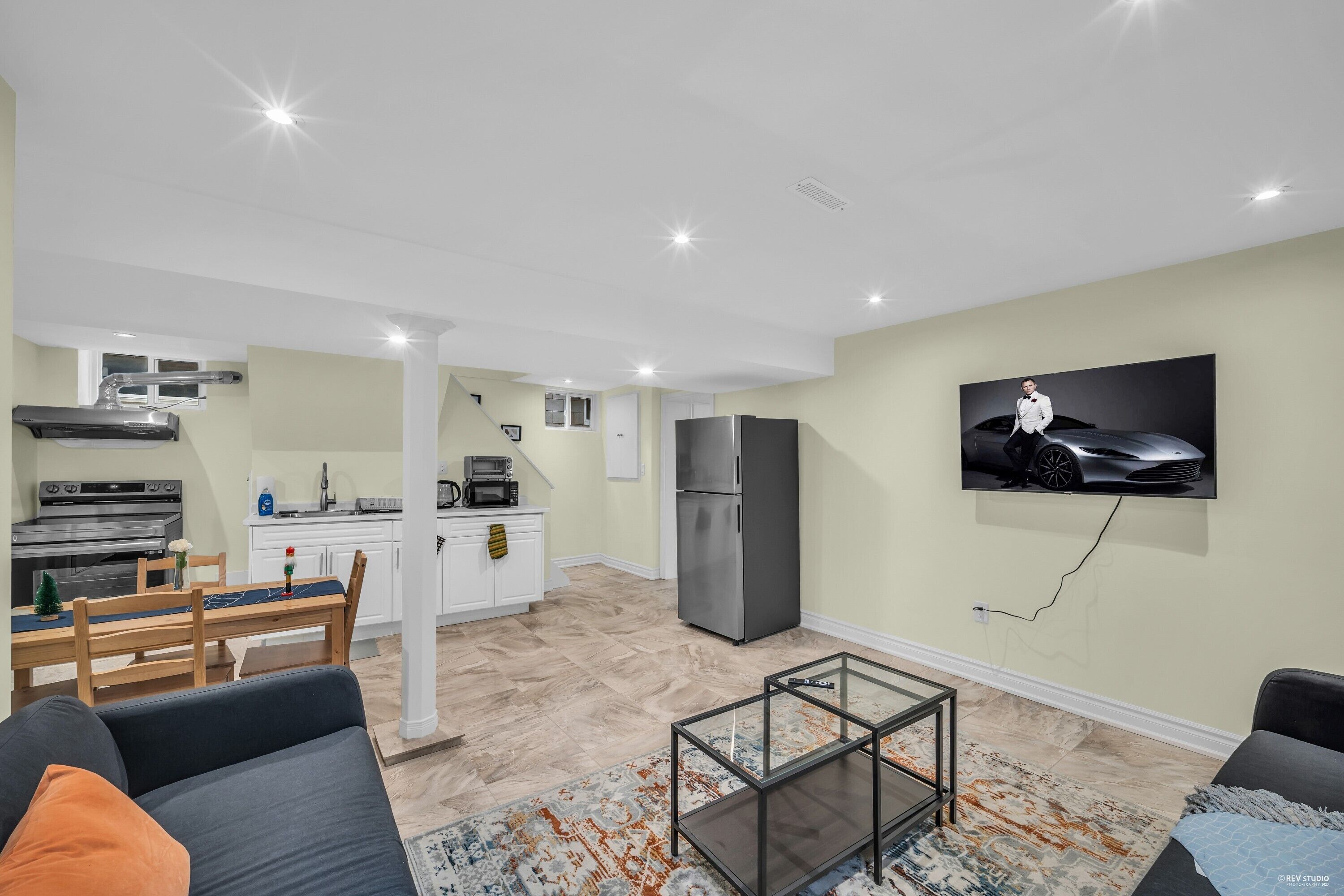 Een moderne woonkamer met een bank, een glazen salontafel en een keukenhoek met een koelkast en magnetron.