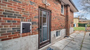 A brick house with a glass door, a small window, and a visible outdoor area with a concrete path. - Spacious 2 Bedroom Guest Suite in North York (Toronto)
