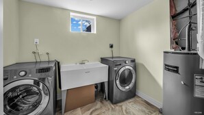 A laundry room with two front-loading washing machines, a sink, and a window with a view of the sky. - Spacious 2 Bedroom Guest Suite in North York (Toronto)