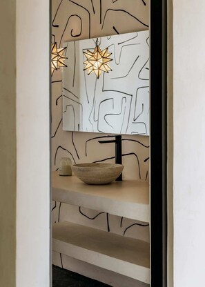 A bathroom with a modern design, featuring a large mirror, a sink with a stone basin, and two star-shaped pendant lights.