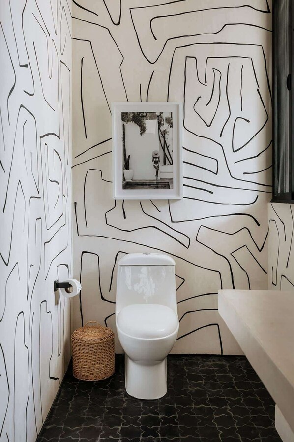 A bathroom with a modern design, featuring a toilet, a framed picture on the wall, and a decorative wall pattern.