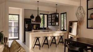 A modern kitchen with a central island, bar stools, pendant lighting, and a dining area with a table and chairs.