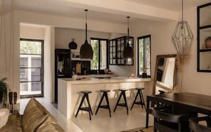 Una cocina moderna con una isla central, taburetes de bar, iluminación colgante y un comedor con mesa y sillas.