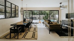 A modern interior with a dining area, sofa, TV, and large windows.