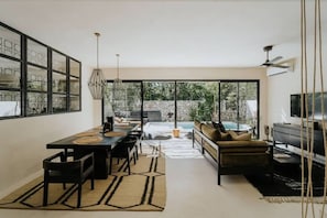 Un interior moderno con zona de comedor, sofá, televisión y ventanas amplias.
