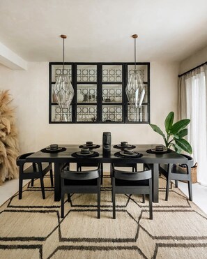 A dining area with a long table, black chairs, a decorative wall piece, and a large plant.