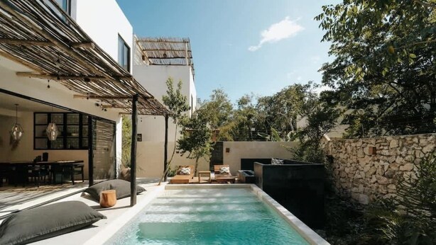 A swimming pool with lounge chairs and a pergola, surrounded by a stone wall and greenery.
