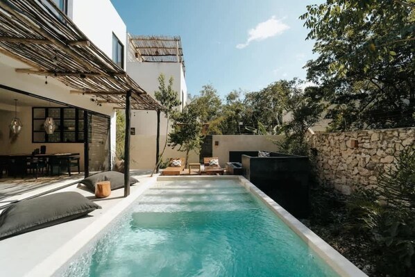 Una piscina con sillones de descanso y una pérgola, rodeada por un muro de piedra y follaje.