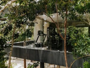 A water feature with a pump and a glass enclosure, surrounded by trees. - Casa Coba Plunge Pool Beach Club Aldea Zama (Tulum)