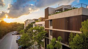 A multi-story building with a modern design, featuring balconies and a parking area with cars. - Jungle Modern Loft 101 Aldea Zama Walk Everywhere (Tulum)