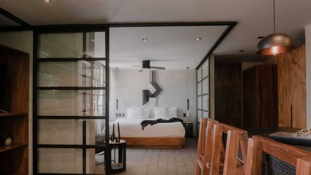 A modern bedroom with a large bed, a ceiling fan, and a view through a glass partition. - Jungle Modern Loft 101 Aldea Zama Walk Everywhere (Tulum)