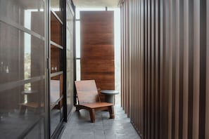 Un couloir étroit, avec un banc en bois et une petite table ronde, qui mène à une pièce dont un des murs est recouvert de panneaux de bois.