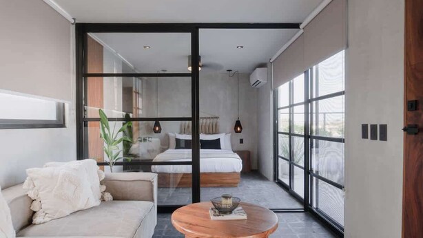 A modern bedroom with a glass door leading to a balcony, a sofa, a round wooden table, and a bed with a view. - Jungle Loft 203 Penthouse Aldea Zama Private Pool (Tulum)