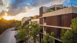 A multi-story building with a modern design, featuring balconies and a parking area with cars. - Jungle Loft 203 Penthouse Aldea Zama Private Pool (Tulum)