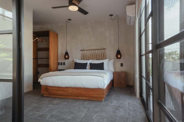 Une chambre à coucher comprenant un lit, un ventilateur de plafond, des lampes suspendues, une armoire et une fenêtre.