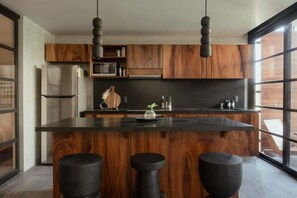 Une cuisine moderne avec des meubles en bois, un îlot central, des tabourets de bar, un four à micro-ondes et des luminaires suspendus.