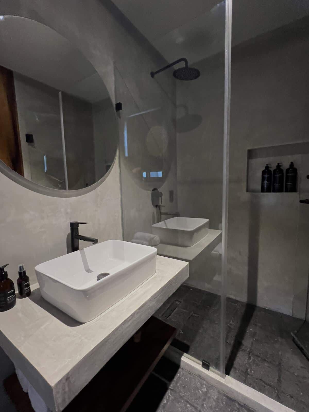 A modern bathroom with a large mirror, two sinks, a shower, and a glass-enclosed shower area.