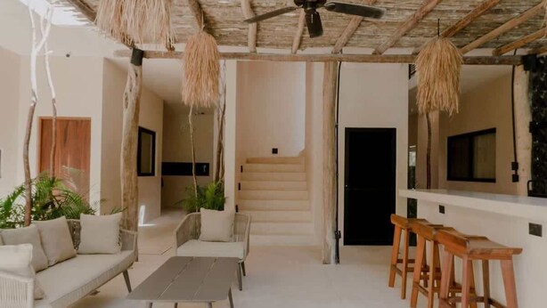 A modern interior with a ceiling fan, wicker furniture, and a staircase leading to a dark door. - Casa Coba Boho Private Pool Beach Club Access (Tulum)