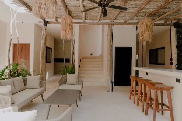 Un intérieur moderne avec un ventilateur de plafond, des meubles en osier et un escalier menant à une porte sombre.