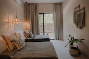 Une chambre à coucher avec un lit, deux tables de chevet, une plante en pot et une vue sur l’extérieur.