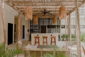 Un espace extérieur abrité, doté d’un toit de chaume, d’un bar avec des tabourets et de mobilier en osier.