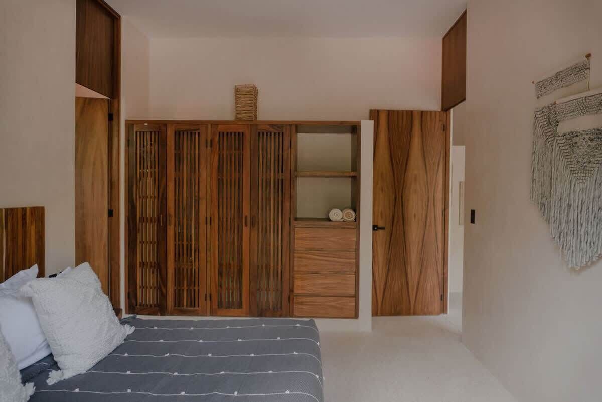 A bedroom with a bed, wooden wardrobe, and a wall-mounted tapestry.
