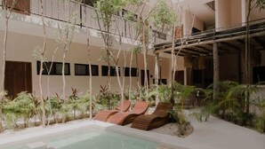 A pool area with lounge chairs, palm trees, and a building with balconies. - Casa Coba Boho Private Pool Beach Club Access (Tulum)