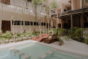 Un espace piscine avec des chaises longues, des palmiers et un bâtiment doté de balcons.