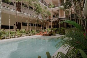 Ein Poolbereich im Innenbereich mit freiem Blick auf den Pool, umgeben von Pflanzen und einer mehrstöckigen Struktur mit Balkonen.