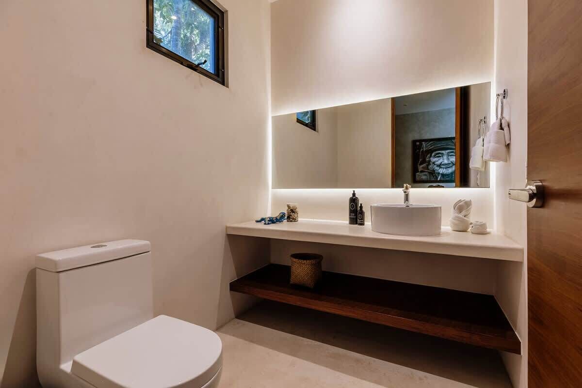 A modern bathroom with a toilet, a sink with a mirror above it, and a small shelf below.