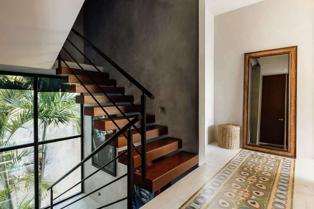 A staircase with wooden steps and black railings, a patterned floor, and a large mirror.