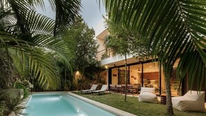 A swimming pool surrounded by lush greenery, a dining area with outdoor seating, and a modern building with large windows. - Casa Iguana Private Villa Large Pool Beach Club (Tulum)