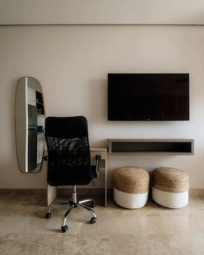 A modern room with a black office chair, a flat-screen TV, a mirror, and two woven ottomans.