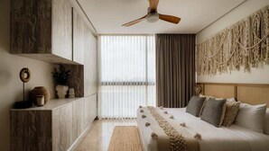 Ein Schlafzimmer mit einem Bett, einem Deckenventilator, einem Fenster mit Vorhängen, einem Holzschrank und einem wandhängenden Wandbehang aus Makramee.