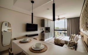 A modern hotel room with a dining area, a flat-screen TV, a sofa, and a large window with a view.