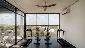 Ein Fitnessstudio mit Trainingsgeräten, großen Fenstern und einem Deckenventilator.